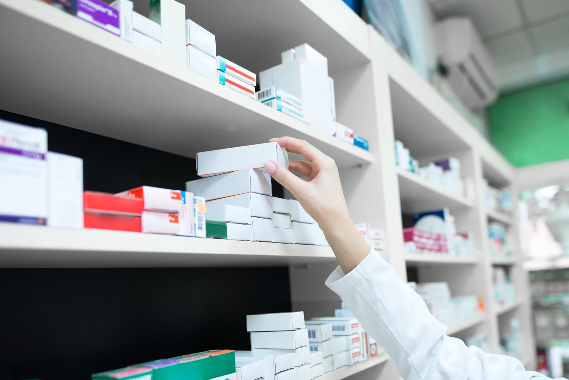 Farmaceutens hand sträcker sig efter en medicinlåda på en hylla fylld med olika läkemedelsförpackningar.