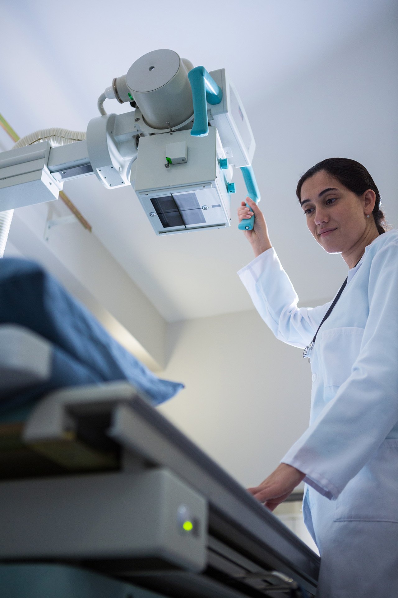 Radiologteknolog som justerar en röntgenmaskin ovanför ett patientbord.