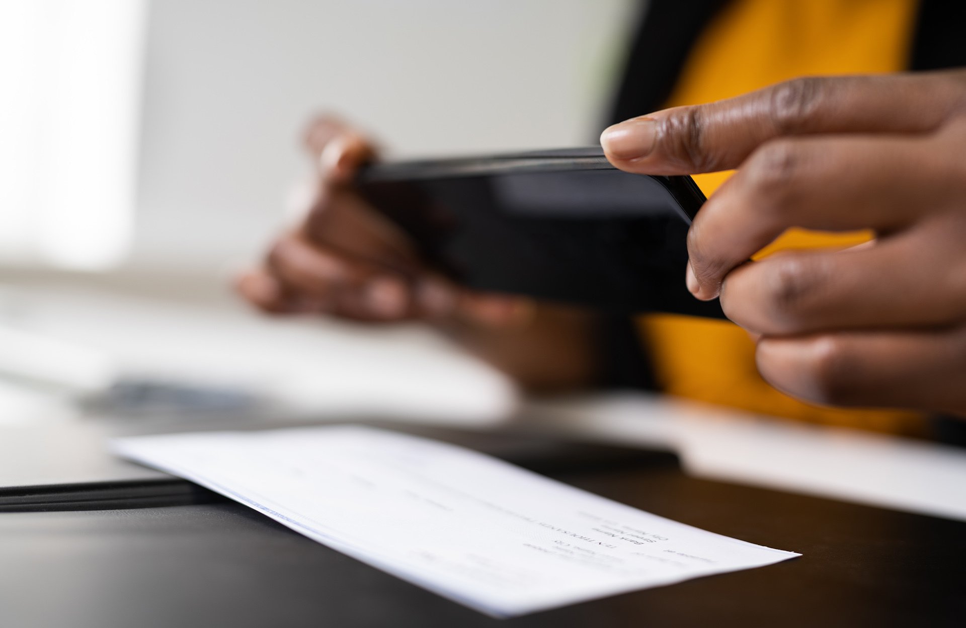Person som tar ett foto av en check med en smartphone för mobil insättning.