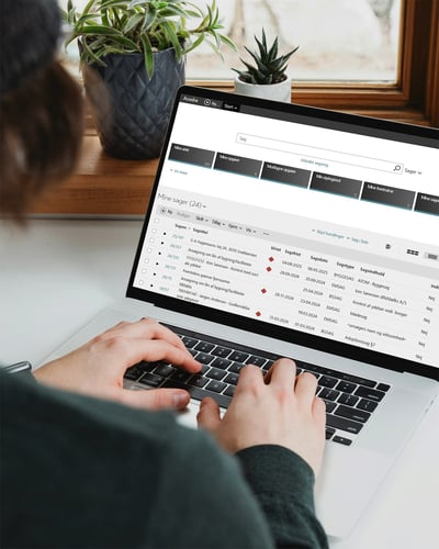 En person skriver på en bärbar dator som visar gränssnittet för Acadre från Formpipe, med uppgiftsdetaljer, deadlines och kategorier i en ljus inomhusmiljö.