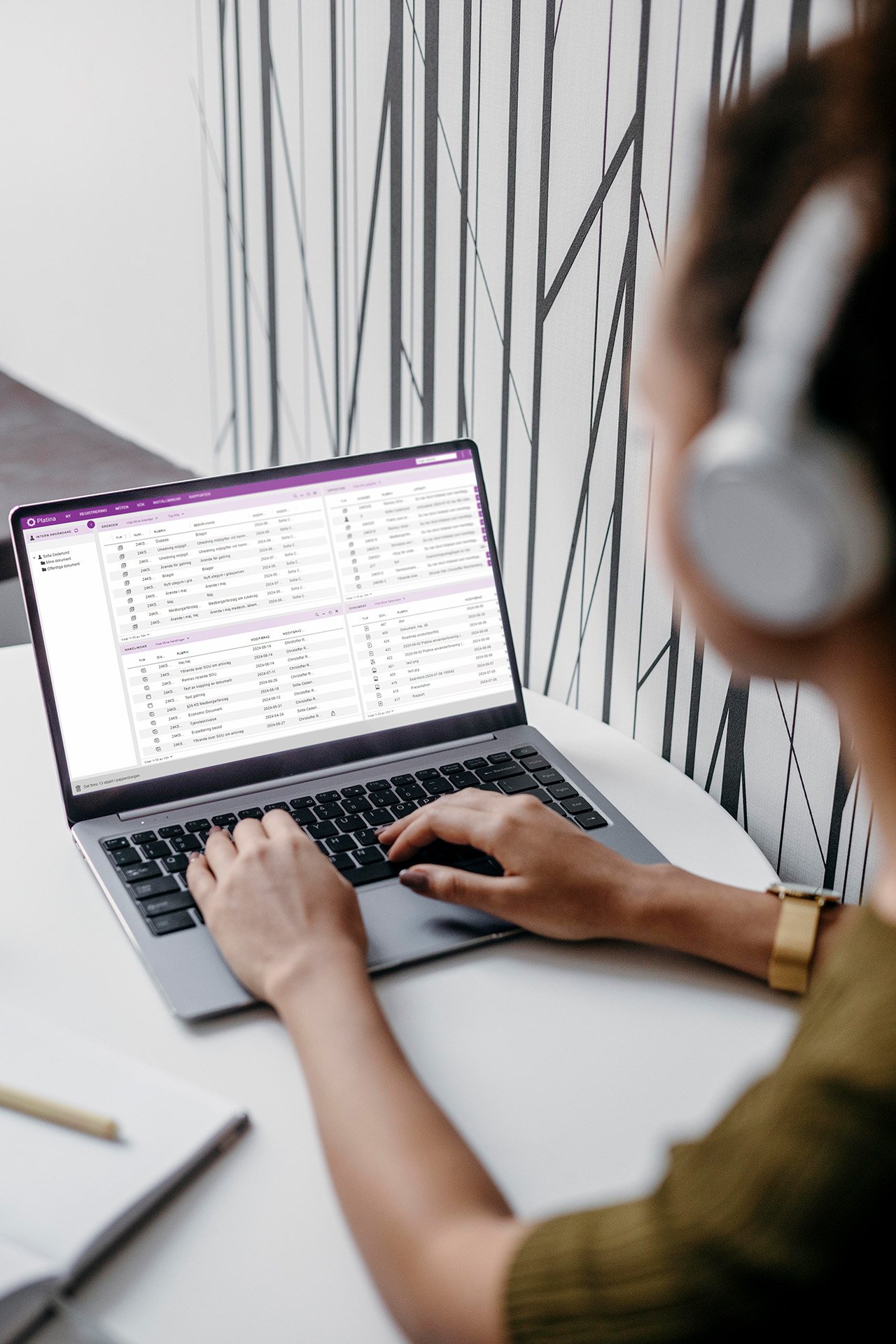 En person med hörlurar skriver på en bärbar dator som visar gränssnittet för Platina från Formpipe, mot en minimalistisk svartvit väggdesign.